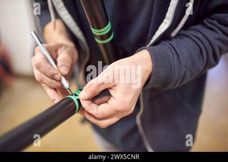 Uomo sconosciuto che prepara il telaio di una bicicletta con un bisturi e nastro di mascheratura per un disegno di pittura personalizzato nella sua officina di bici. Foto Stock