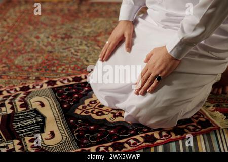 Vista dall'alto dell'irriconoscibile giovane musulmano che indossa un abito bianco che fa il namaz sul tappeto di preghiera, copia spazio Foto Stock