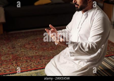 Foto ad angolo alto di un uomo musulmano barbuto in abiti bianchi seduti su un tappeto che prega salah, copia spazio Foto Stock