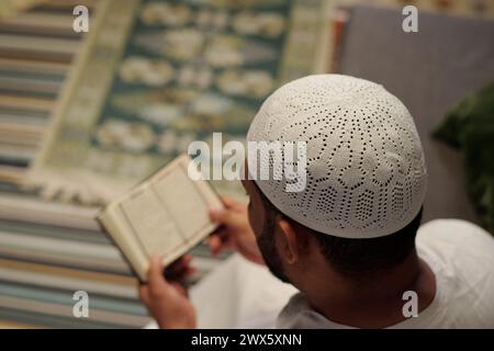 Ripresa selettiva con vista ad alto angolo dell'irriconoscibile uomo musulmano che indossa taqiyah bianca che legge il Corano, copia spazio Foto Stock