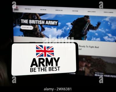 Persona che possiede uno smartphone con il logo della forza di terra britannica British Army davanti al sito web. Mettere a fuoco il display del telefono. Foto Stock