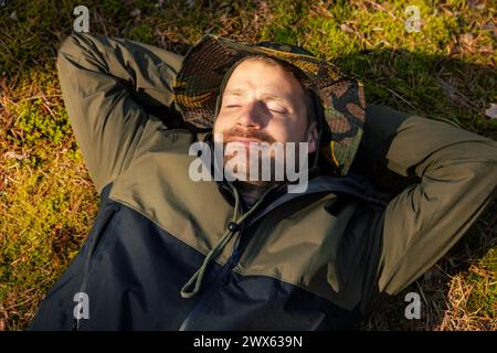 uomo tranquillo e soddisfatto che dorme e riposa sul muschio verde della foresta. fuga dalla natura e tranquillità. sollievo dallo stress e salute mentale Foto Stock