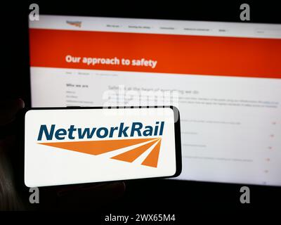 Persona che possiede uno smartphone con il logo della società di infrastrutture ferroviarie Network Rail Limited davanti al sito web. Mettere a fuoco il display del telefono. Foto Stock