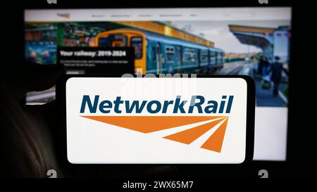 Persona che detiene un cellulare con il logo della società di infrastrutture ferroviarie Network Rail Limited di fronte alla pagina web aziendale. Mettere a fuoco il display del telefono. Foto Stock