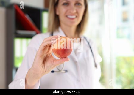 Nutrizionista femminile sorridente tiene in mano frutta fresca di pesca da vicino. Foto Stock