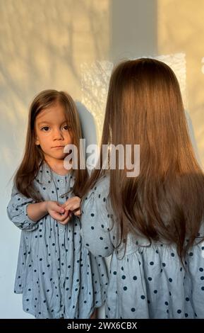 Una delle due ragazze gemelle in abito blu in piedi davanti mentre sua sorella guarda la macchina fotografica su sfondo bianco Foto Stock