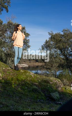 Donna che cammina nella natura con uno zaino e vestita di pesca e azzurro Foto Stock