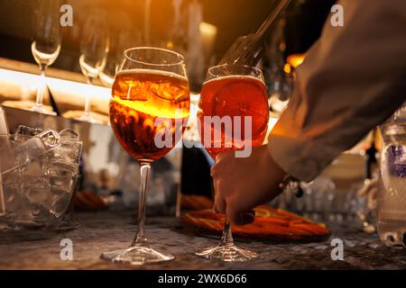 Il barista prepara due bicchieri di cocktail Aperol spritz sul bancone del bar e aggiunge fette d'arancia fresche. Tipica bevanda alcolica italiana, aperitivo a base di Foto Stock