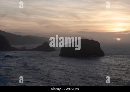 tramonto sereno sull'oceano, che mette in risalto le isole sagomate e illumina il cielo con tonalità calde e morbide Foto Stock