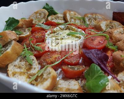 Formaggio Camembert al forno con pomodori e baguette, erbe aromatiche, rucola e spinaci. Ottimo spuntino da accompagnare con il vino. Foto Stock