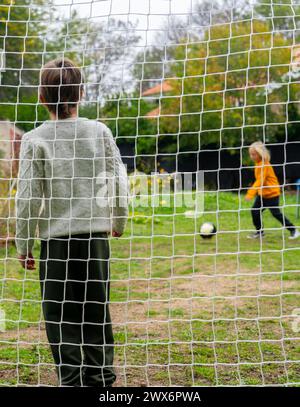 Due bambini che giocano a calcio, uno che tira in porta e l'altro come portiere Foto Stock