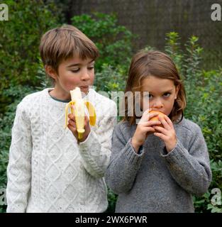 due bambini mangiano frutta (banana e mela) all'aperto Foto Stock