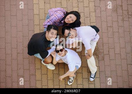 Gruppo di amici allegri seduti in squat e sorridenti alla telecamera, vista dall'alto Foto Stock
