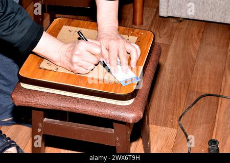 Riparazione di mobili. Il falegname apporta dei contrassegni sulla tavola del sedile della sedia per i fori futuri. Foto Stock