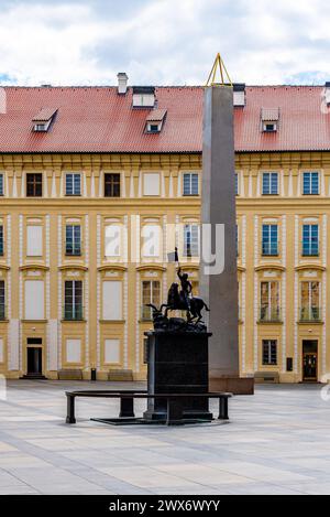 San Giorgio a cavallo, trionfando su un drago, si erge davanti a un obelisco nello storico cortile del castello di Praga con un'elegante facciata sullo sfondo. Praga, Cechia Foto Stock