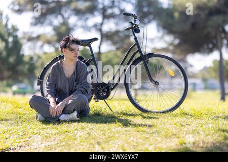 Una donna siede sull'erba accanto a una bicicletta nera Foto Stock
