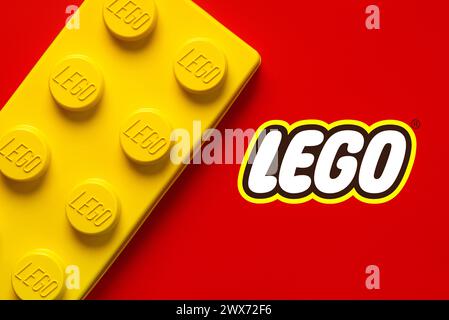 Primo piano di un grande blocco lego giallo con il logo Lego su sfondo rosso. Editoriale illustrativo Foto Stock