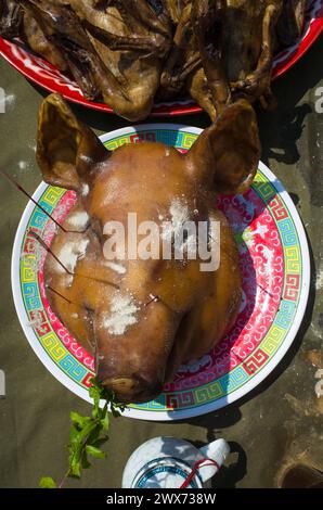 Grande testa di maiale cotta sul piatto sul tavolo, tra gli altri piatti offerti a Dio al Capodanno cinese nell'isola di Koh Tao, Thailandia Foto Stock