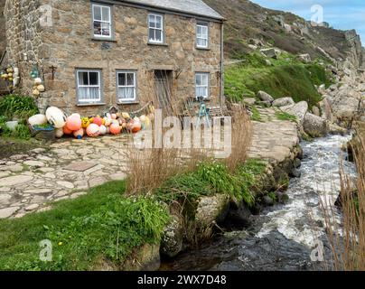 Grazioso vecchio cottage sul mare in pietra granitica della Cornovaglia vicino al ruscello con galleggianti da pesca e boe a Penberth Cove, Cornovaglia, Regno Unito Foto Stock