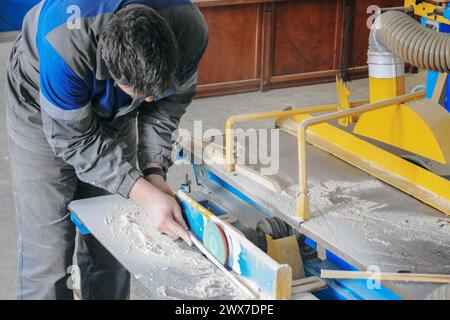 Un uomo sta lavorando a un progetto di lavorazione del legno, usando una sega per tagliare un pezzo di legno. Foto Stock