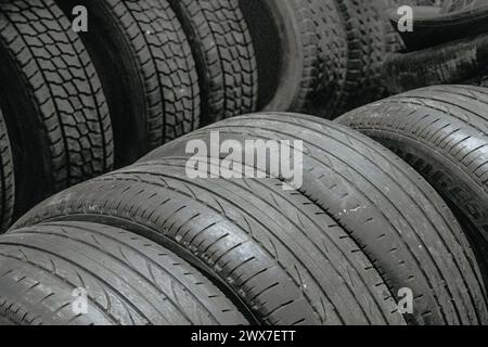 Un mucchio di vecchi pneumatici impilati uno sopra l'altro. Gli pneumatici sono neri e sembrano usurati Foto Stock