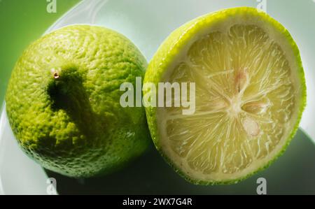 Mezze limoni freschi e succosi tagliati su sfondo verde, luce laterale che entra dalla finestra. Foto Stock
