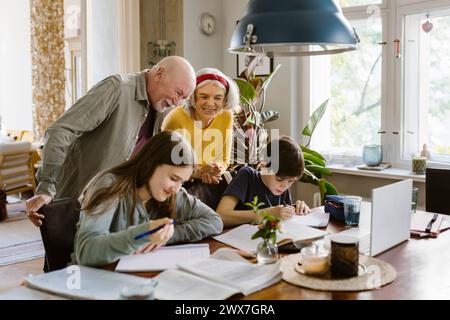 Nonni sorridenti con nipoti che studiano a casa Foto Stock