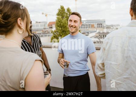 Amici uomini e donne felici che si godono un drink alla festa in balcone Foto Stock