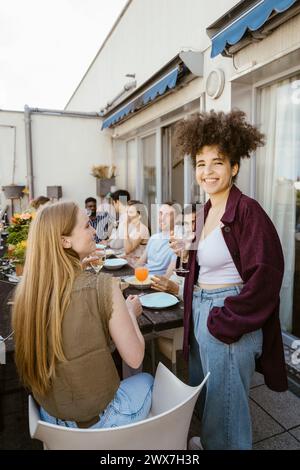 Sorridente giovane donna che si gusta cibo e bevande con gli amici a cena sul balcone Foto Stock