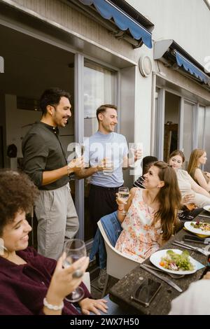 Amici maschi sorridenti che sorseggiano un drink con un gruppo di amici a cena sul balcone Foto Stock
