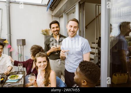 Amici maschi felici con un gruppo di amici che si godono un drink durante la cena in balcone Foto Stock