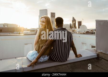 Ritratto di donna sorridente che guarda a spalla mentre siede con il fidanzato sulla terrazza dell'edificio Foto Stock