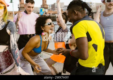 Persona felice non-binaria che indossa occhiali da sole e balla con gli amici in città Foto Stock