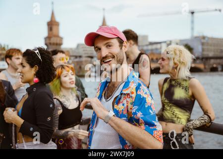 Ritratto di un uomo gay sorridente che indossa motivi floreali e danza con amici non binari in città Foto Stock