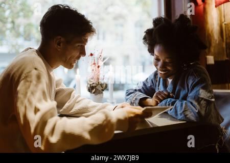 Fidanzato che suggerisce un piatto alla fidanzata che guarda il menù al ristorante Foto Stock