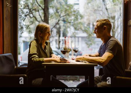 Una coppia matura sorridente si guarda mentre beve del vino al bar Foto Stock