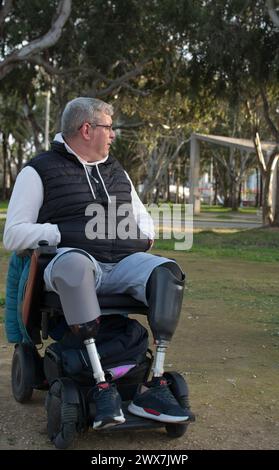 un uomo senza gambe in sedia a rotelle posa nel parco, guardando l'orizzonte. Foto Stock