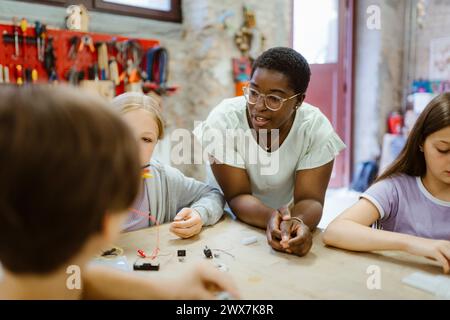 Insegnante donna appoggiata sul tavolo mentre insegna agli studenti durante la lezione di tecnologia Foto Stock