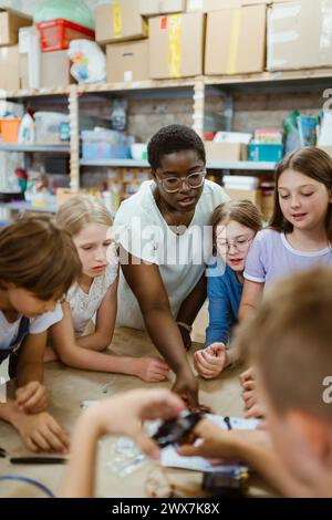 Insegnante donna che assiste il gruppo di studenti che lavorano al progetto di robotica in officina Foto Stock