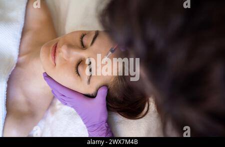 Vista dall'alto di una donna che riceve un'iniezione di riempitivo botox anti-invecchiamento sulla fronte da un cosmetologo professionista nel salone di bellezza. Trattamento viso e. Foto Stock