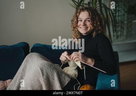 Giovane donna felice che si diverte a lavorare a maglia a casa in un salotto, a fare attività ricreative e a fare hobby nel tempo libero. Uncinetto in cotone artigianale. Foto Stock