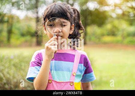 Una giovane ragazza che regge una lente d'ingrandimento su un pezzo di carta Foto Stock