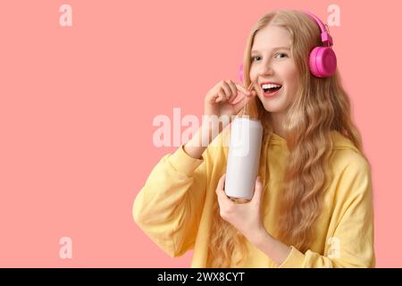 Bella giovane donna con le cuffie con lattina di bibita su sfondo rosa Foto Stock