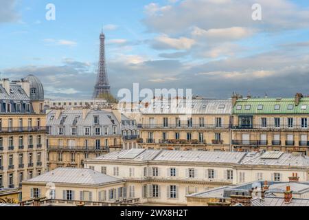 Una vista di Parigi con l'iconica Torre Eiffel che si innalza sopra i tetti classici sotto un cielo nuvoloso. Parigi, Francia Foto Stock