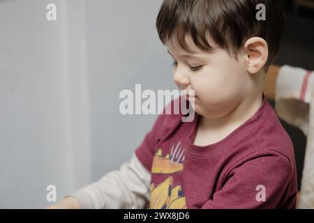 un ragazzo curioso che gioca con un tagliapiedi giocattolo al tavolo della cucina Foto Stock