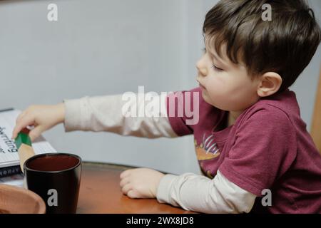 un ragazzo curioso che gioca con un tagliapiedi giocattolo al tavolo della cucina Foto Stock