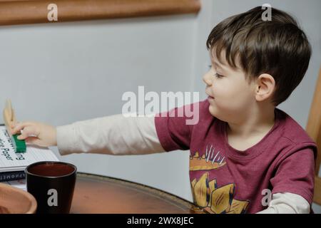 un ragazzo curioso che gioca con un tagliapiedi giocattolo al tavolo della cucina Foto Stock