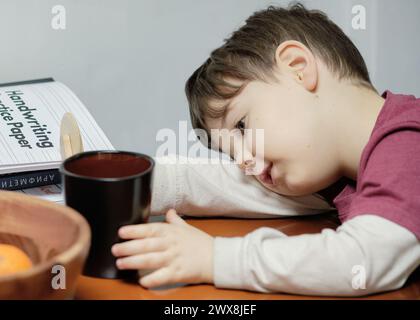 un ragazzo curioso che gioca con un tagliapiedi giocattolo al tavolo della cucina Foto Stock