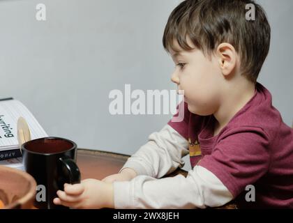 un ragazzo curioso che gioca con un tagliapiedi giocattolo al tavolo della cucina Foto Stock