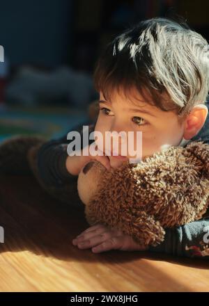 bambino che abbraccia un orso giocattolo nella stanza dei bambini durante il pisolino Foto Stock